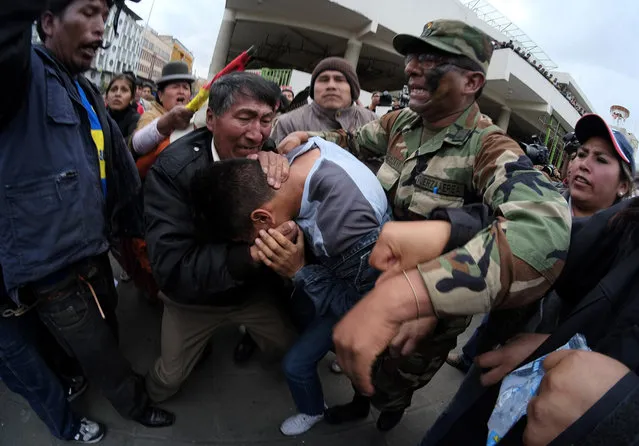A intelligence officer (C) who infiltrated the protest of Bolivia's low ranking army officers protects himself from demonstrators at the San Francisco square in La Paz, April 29, 2014. Hundreds of low ranking officers of Bolivia's Armed Forces continue to protest after Bolivia's military leaders dismissed hundreds of soldiers for “sedition”, according to local media. Picture taken with fisheye lens. (Photo by David Mercado/Reuters)