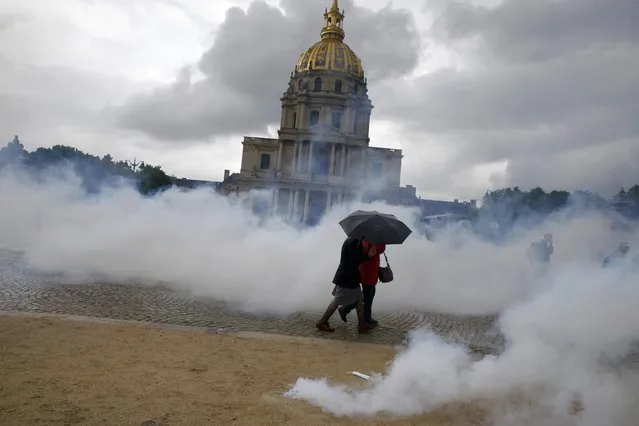 Clouds of tear gas surround people who walk with an umbrella near the Invalides monument during clashes between protestors and French police during a demonstration against French labour law reform in Paris, France, May 12, 2016. (Photo by Gonzalo Fuentes/Reuters)