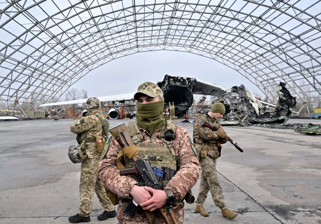 Ukrainian servicemen stand guard in front of a destroyed Ukrainian Antonov An-225 “Mriya”, the largest cargo aircraft in the world, at an aerodrome in Hostomel, during a donation ceremony of some ten off-road vehicles mounted with machine guns, from volunteers project HEROCAR for mobile fire groups of air defense to resist drones attacks, on April 1, 2023, amid the Russian invasion of Ukraine. (Photo by Sergei Supinsky/AFP Photo)