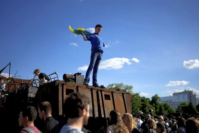 A boy holds a Ukrainian flag on a destroyed Russian tank placed as a symbol of war during Kyiv Day celebrations in downtown Kyiv, Ukraine, Sunday, May 29, 2022. (Photo by Natacha Pisarenko/AP Photo)