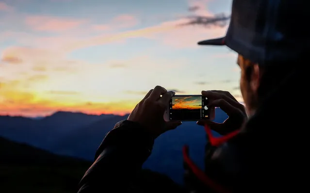 A man takes a picture with his smartphone during sunrise on Kreuzjoch mountain in the Zillertal Alps in Schwendau, Austria July 11, 2016. (Photo by Dominic Ebenbichler/Reuters)