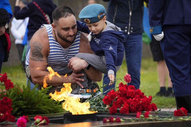 A former paratrooper and his son place flowers at an eternal flame during celebration for Paratroopers' Day in St. Petersburg, Russia, Tuesday, August 2, 2022. Paratroopers are an elite unit of the Russian Army, and everyone in the country recognizes their blue berets. (Photo by Dmitri Lovetsky/AP Photo)