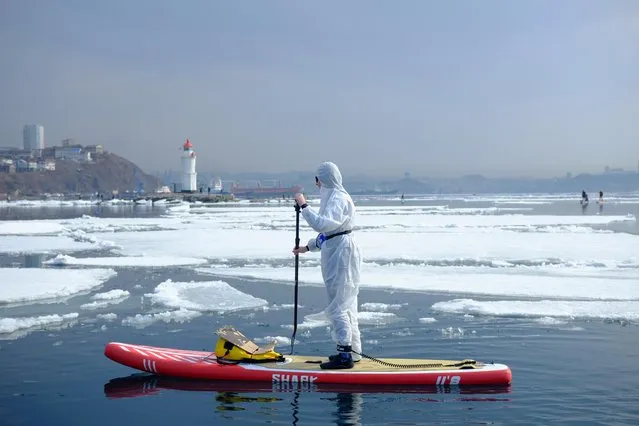 A sup surfer wearing a protective suit as a show of support for the people fighting against the spread of coronavirus disease takes part at an annual “Hijacking an ice floe” event marking the opening of the stand up paddle boarding season in Vladivostok, Russia on March 21, 2020. (Photo by Ivan Belozyorov/Reuters)
