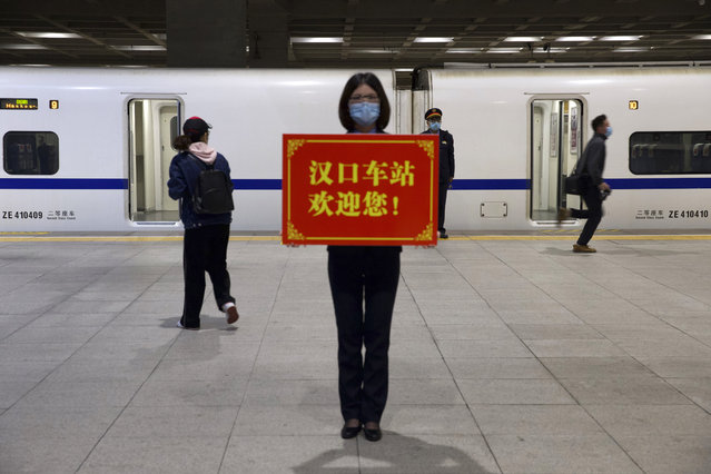 A railway worker holds a sign reading "Hankou Station welcomes you!" as passengers board the first high-speed train to leave Hankou train station after the resumption of train services in Wuhan in central China's Hubei Province, Wednesday, April 8, 2020. (Photo by Ng Han Guan/AP Photo)