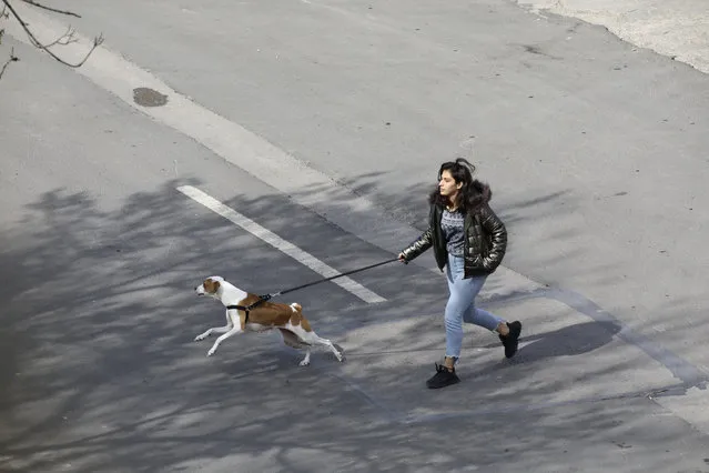 A woman walks her dog in a deserted street amid the coronavirus outbreak, in Ankara, Turkey, Sunday, March 22, 2020. (Photo by Burhan Ozbilici/AP Photo)