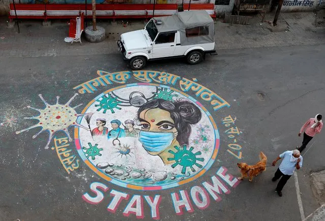 A man walks his dog past a graffiti on a road to create awareness about staying at home during an extended nationwide lockdown to slow the spreading of coronavirus disease (COVID-19) in Lucknow, April 22, 2020. (Photo by Pawan Kumar/Reuters)
