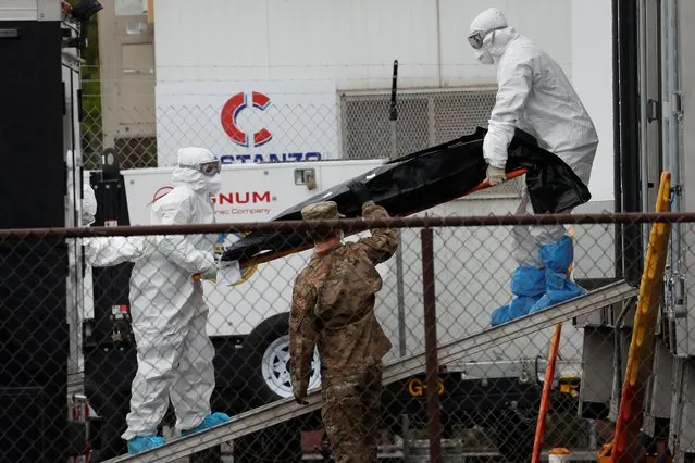 Workers wearing personal protective equipment (PPE) move the body of a deceased person from a refrigerated truck trailer set up at a temporary morgue outside University Hospital during the outbreak of the coronavirus disease (COVID-19) in Newark, New Jersey, U.S., May 6, 2020. (Photo by Mike Segar/Reuters)