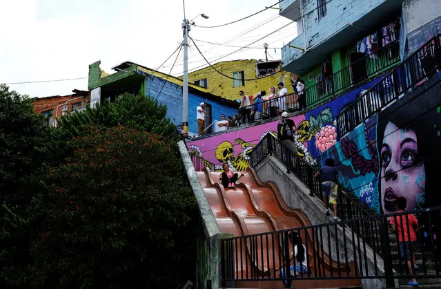 Tourists (top) stand as residents play on a slide, next to a public outdoor escalator in the “Comuna 13” neighborhood in Medellin, Colombia on September 16, 2017. (Photo by Nacho Doce/Reuters)