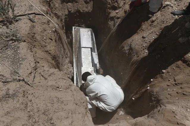 A worker wearing a protection suit against the spread of the new coronavirus buries a coffin in an area of the San Rafael municipal cemetery set apart for COVID-19 cases in Ciudad Juarez, Mexico, Tuesday, May 19, 2020. (Photo by Christian Chavez/AP Photo)