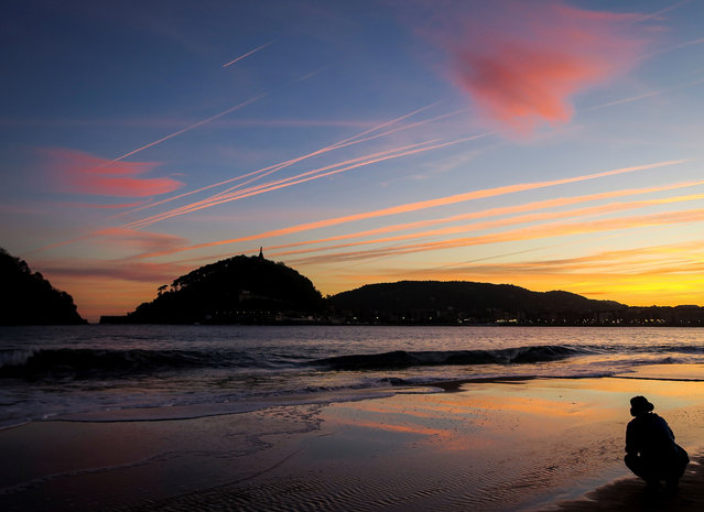 A man looks as the sun rises over the beach of Ondarreta in San Sebastian, in the northeren region of the Basque Country, Spain, 24 October 2017. The city of San Sebastian is experiencing hot temperatures up to 28 degrees Celsius. (Photo by Javier Etxezarreta/EPA/EFE)