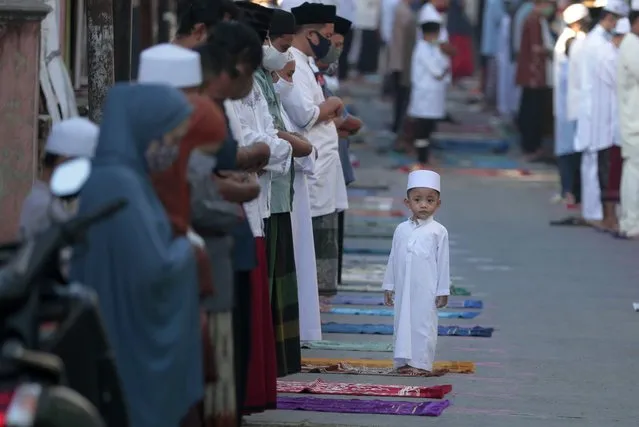 A boy stands as his parents perform an Eid al-Fitr prayer marking the end of the holy fasting month of Ramadan amid concerns of the new coronavirus outbreak in Jakarta, Indonesia, Sunday, May 24, 2020. (Photo by Dita Alangkara/AP Photo)