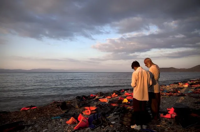 Two Syrian refugees stand on a beach amidst life jackets and deflated dinghies, moments after arriving in a dinghy on the Greek island of Lesbos, September 13, 2015. Tens of thousands of mainly Syrian refugees have braved rough seas this year to make the short but precarious journey from Turkey to Greece's eastern islands, mainly in flimsy and overcrowded inflatable dinghies. (Photo by Alkis Konstantinidis/Reuters)