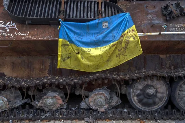 A Ukrainian flag with messages of support for cities of eastern Ukraine hangs from a destroyed Russian tank displayed in downtown Kyiv, Ukraine, Monday, November 7, 2022. (Photo by Bernat Armangue/AP Photo)