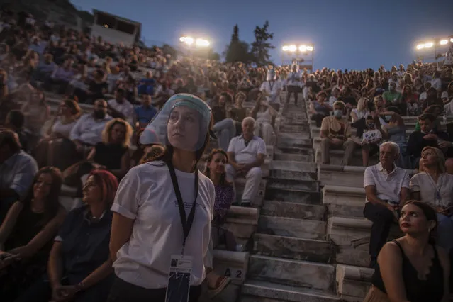 An usherette wearing a face shield stands in front of the audience at the Odeon of Herodes Atticus in Athens, Greece, after the site was reopened for performances on Wednesday, July 15, 2020. Seating limits have been imposed at the renovated ancient stone Roman theater, underneath the Acropolis, as part of the restrictions due to the COVID-19 pandemic. Authorities allowed the venue to reopen despite recently canceling some other summer events to avoid crowding. (Photo by Petros Giannakouris/AP Photo)