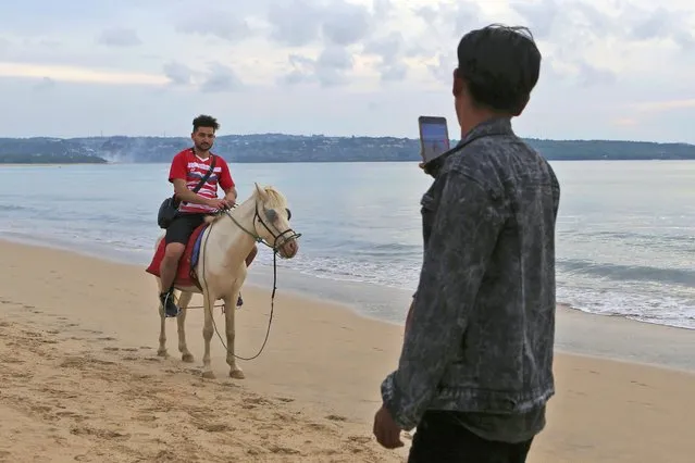 A foreign tourist on a horse has his photo taken on Jimbaran Beach, Bali, Indonesia on Friday, November 11, 2022. The dozens of world leaders and other dignitaries traveling to Bali for the G-20 summit will be drawing a welcome spotlight on the revival of the tropical island's ailing tourism sector after a two-year closure to foreign travelers due to the pandemic. (Photo by Firdia Lisnawati/AP Photo)