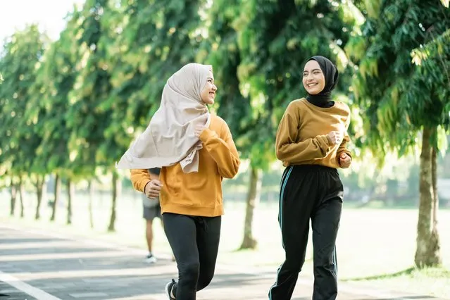 Two asian muslim girls enjoy jogging together while chatting in the afternoon in the garden field. (Photo by Odua Images/Rex Features/Shutterstock)
