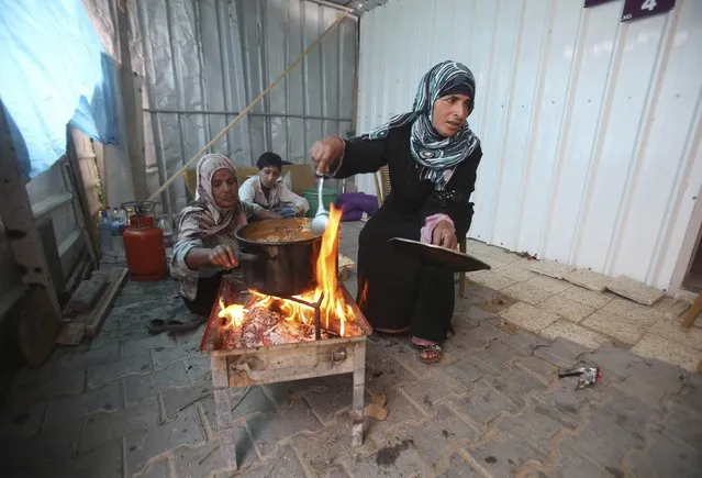 Palestinians, who live in a container as a temporary replacement for their house that witnesses said was destroyed by Israeli shelling during the most recent conflict between Israel and Hamas, cook on a fire on a rainy day in the east of Khan Younis in the southern Gaza Strip November 16, 2014. (Photo by Ibraheem Abu Mustafa/Reuters)
