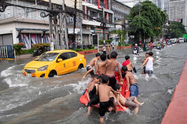 Children play along a flooded street in Manila on July 21, 2025, after Typhoon Wipha brought heavy rains and flooding to the Philippines, where two people have been reported missing, according to the country's National Disaster Risk Reduction and Management Council.  (Photo by Ted Aljibe/AFP Photo)