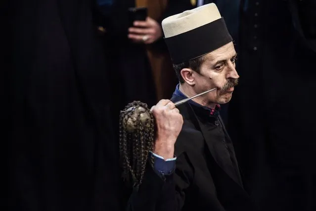 A Kosovo dervish, adept of Sufism, a mystical form of Islam, pierces his cheek with a needle during a ceremony in a prayer room in Prizren on March 22, 2018 during Newroz celebrations. The Kosovo dervish community carries on centuries-old mystical practices, such as self-piercing with needles and knives as a way to earn salvation and find the path to God. Newroz (also known as Nawroz or Nowruz) is an ancient Persian festival, marking the first day of spring, which falls on March 21. (Photo by Armend Nimani/AFP Photo)
