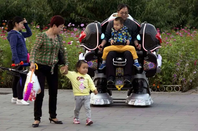 A man rides a mechanical robot with a child at a park in Beijing, China, Friday, September 30, 2016. China's decision to change its one child policy and allow all married couples to have two children is expected to contribute to the country's long term economic growth and provide future relief for its greying population. (Photo by Ng Han Guan/AP Photo)