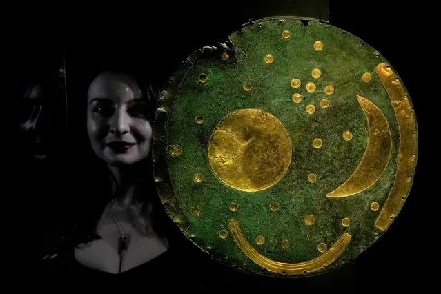 A member of staff poses next to the “Nebra Sky Disc” which dates from around 1600 BCE, and is the oldest surviving representation of the cosmos, on display at the The World of Stonehenge' exhibition at the British Museum in London, Monday, February 14, 2022. The exhibition which displays objects and artifacts from the era of Stonehenge opens 17, Feb. and runs until 17, July 2022. The Nebra Disc was found in Nebra in Saxony-Anhalt in east Germany, in 1999. (Photo by Alastair Grant/AP Photo)