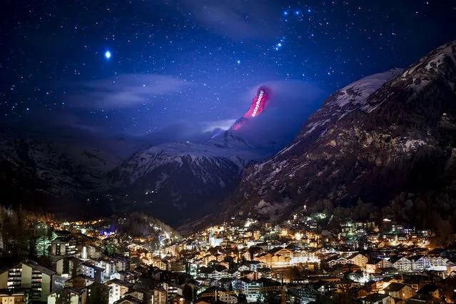 The iconic Matterhorn mountain is illuminated by Swiss light artist Gerry Hofstetter aiming to send messages of hope, support and solidarity to the ones sufferings from the global coronavirus disease, COVID-19, pandemic in the alpine resort of Zermatt, Switzerland, Thursday, March 26, 2020. (Photo by Valentin Flauraud/Keystone via AP Photo)