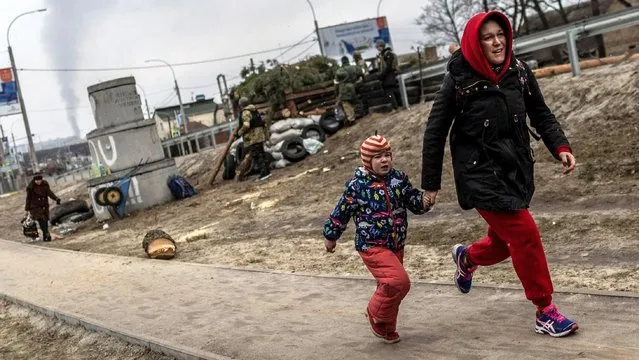 Local residents run for cover as they escape from the town of Irpin, after heavy shelling on the only escape route used by locals, while Russian troops advance towards the capital of Kyiv, in Irpin, near Kyiv, Ukraine on March 6, 2022. (Photo by Carlos Barria/Reuters)