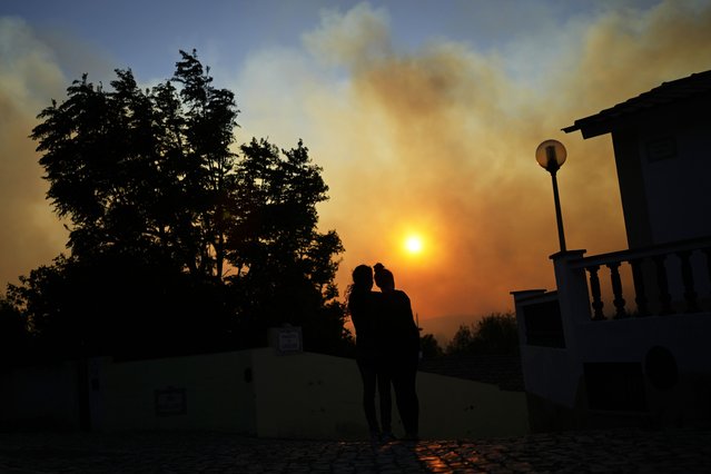 Two women watch a wildfire burning near houses in Alcabideche, outside Lisbon, Tuesday, July 25, 2023. Hundreds of firefighters and over a dozen airplanes were fighting a wildfire that spread quickly fanned by strong winds. (Photo by Armando Franca/AP Photo)