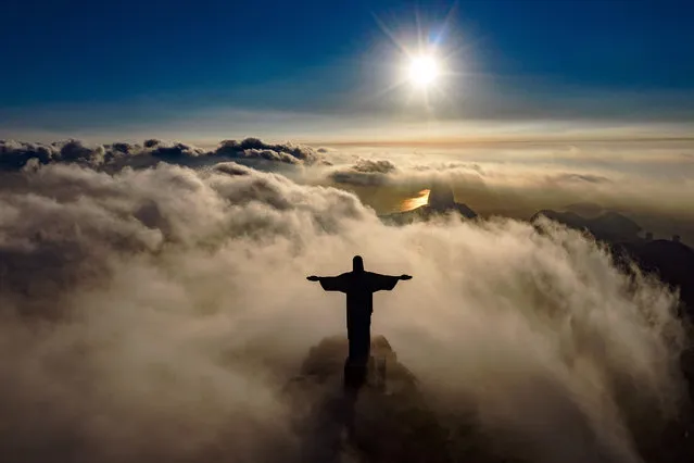The sun rises in front of the Christ the Redeemer statue in Rio de Janeiro on March 24, 2021. Christ the Redeemer is celebrating its 90th anniversary in October 2021 and is receiving restoration work to ensure that it looks its best for the public and visiting tourists. (Photo by Carl de Souza/AFP Photo)