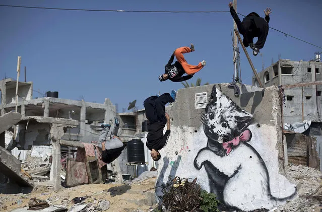 Palestinian youths practice their Parkour skills past a mural said to have been painted by British street artist Banksy, on the remains of a house that was destroyed during the 50-day war between Israel and Hamas militants in the summer of 2014, in the Gaza Strip town of Beit Hanun on March 13, 2015. (Photo by Mohammed Abed/AFP Photo)