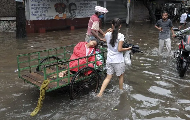 A sick person is taken on a cycle cart to see a doctor through a waterlogged street following heavy rains in Kolkata, India, Thursday, June 17, 2021. (Photo by Ashim Paul/AP Photo)