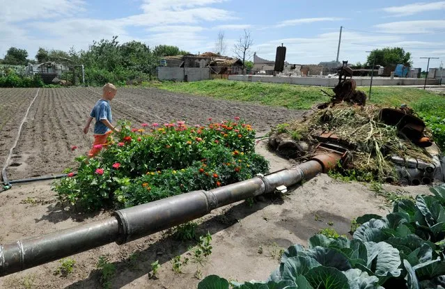 A boy walks in a kitchen-garden past remains of a Russian battle tank, destroyed during battles this spring, in the village of Velyka Dymerka, northeast of Kyiv,  outside of Kyiv, on July 21, 2022, amid the Russian invasion of Ukraine. (Photo by Sergei Chuzavkov/AFP Photo)