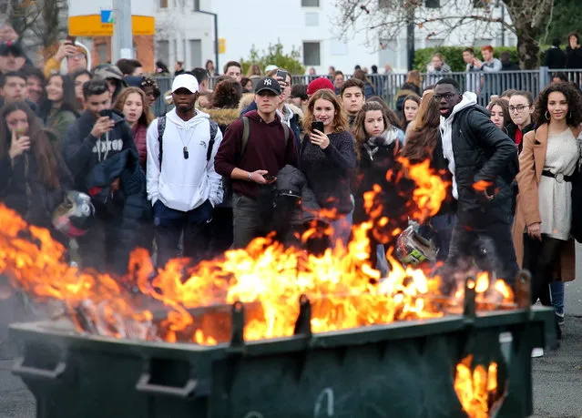 Students watch a burning trash bin outside their school in Bayonne, southwestern France, Thursday, December 6, 2018. Protesting students are disrupting schools and universities Thursday, and drivers are still blocking roads around France, now demanding broader tax cuts and government aid. (Photo by Bob Edme/AP Photo)