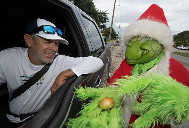 In this photo provided by the Florida Keys News Bureau, a motorist examines the option of receiving an onion instead of a traffic citation from Monroe County Sheriff's Office Colonel Lou Caputo, right, costumed as the Grinch, Friday, December 22, 2023, in Key Largo, Fla. In a holiday tradition, begun by Caputo more than 20 years ago, drivers lightly speeding or talking on a cellular phone in a school zone on the Florida Keys Overseas Highway can choose to receive an onion rather than a $300 citation from the Grinch. (Photo by Andy Newman/Florida Keys News Bureau via AP Photo)