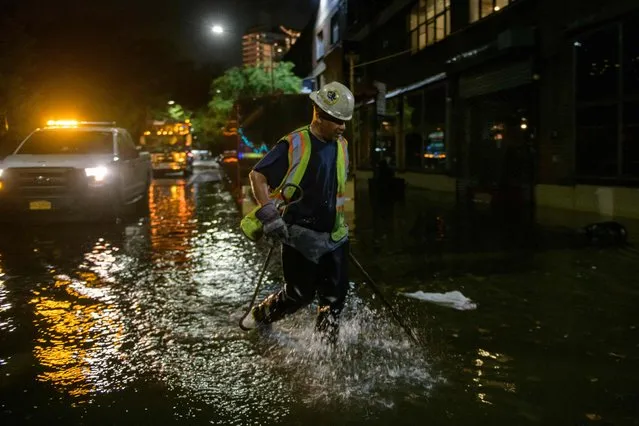 A worker unblocks drains on a street affected by floodwater in Brooklyn, New York early on September 2, 2021, as flash flooding and record-breaking rainfall brought by the remnants of Storm Ida swept through the area. (Photo by Ed Jones/AFP Photo)