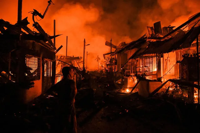 This picture taken at late night on October 1, 2021 shows a resident (L) looking at the charred remains of his home during a fire that also gutted pre-World War II era shoplots in Karak, Malaysia's Pahang state. (Photo by Mohd Rasfan/AFP Photo)
