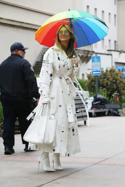Heidi Klum is pictured arriving to America's Got Talent in Los Angeles on March 23, 2024. The 50 year old model and television host wore a long white trench coat with a large white handbag, white leather boots and a bright rainbow color umbrella. (Photo by The Image Direct)