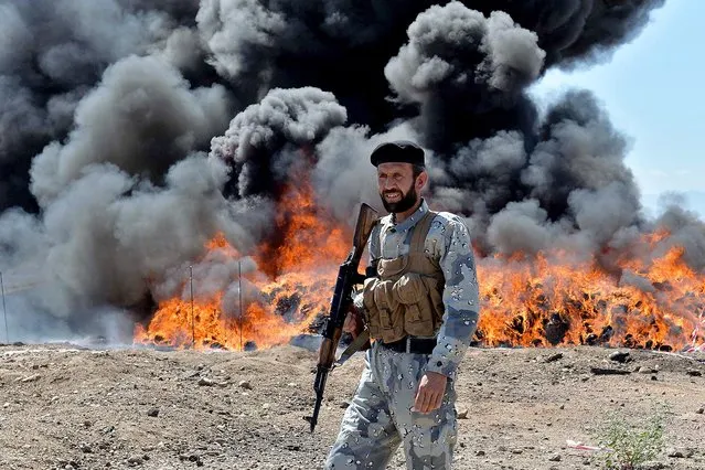 An Afghan security personnel stands guard as seized drugs and alcoholic drinks burn on the outskirts of Jalalabad in eastern Afghanistan on May 28, 2019. More than 14 tons of opium, heroin, hashish and alcoholic drinks were set ablaze by officials which were seized during six months operations, officials said. (Photo by Noorullah Shirzada/AFP Photo)