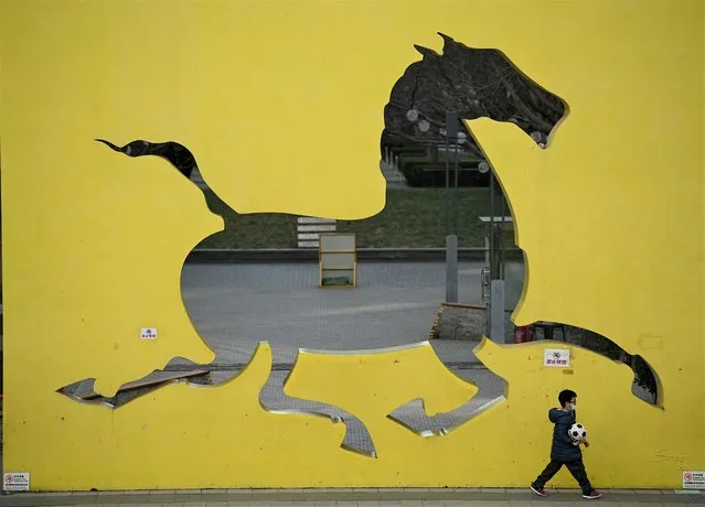 A boy walks in front of a horse sculpture in a park in Beijing on December 20, 2021. (Photo by Noel Celis/AFP Photo)