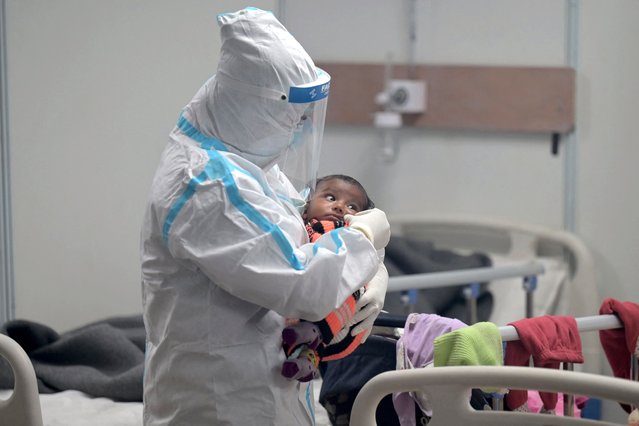A health worker wearing a Personal Protective Equipment (PPE) suit comforts a child infected with Covid-19 coronavirus inside a ward at the Commonwealth games (CWG) village sports complex, temporarily converted into Covid-19 coronavirus care centre, in New Delhi on January 5, 2022. (Photo by Money Sharma/AFP Photo)