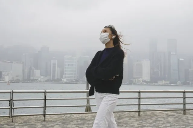 A woman wearing a face mask walks along a street in Hong Kong, Friday, January 28, 2022. Hong Kong is cutting the length of mandatory quarantine for people arriving from overseas from 21 to 14 days, even as the southern Chinese city battles a new surge in COVID-19 cases. (Photo by Kin Cheung/AP Photo)