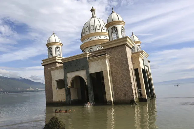 In this Wednesday, April 3, 2019, photo, children play in the water on a beach near a mosque collapsed during Sept. 28, 2018, earthquake is seen in the background in Palu, Central Sulawesi, Indonesia. The earthquake spawned a large localized tsunami that wiped out coastal areas, while liquefaction caused by the shaking turned entire neighborhoods into rivers of sludge. The disaster killed thousands of people, making it the world’s deadliest seismic event in 2018. (Photo by Tatan Syuflana/AP Photo)