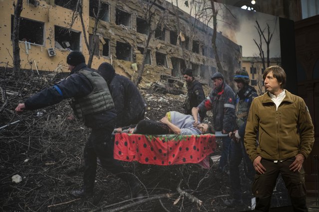 World Press Photo of the Year award winner, Associated Press photographer Evgeniy Maloletka, poses in front of his winning image of a pregnant woman being carried through the wreckage of a maternity hospital after a Russian military strike in Mariupol, Ukraine, prior to a press conference announcing the winners in Amsterdam, Netherlands, Thursday, April 20, 2023. (Photo by Peter Dejong/AP Photo)