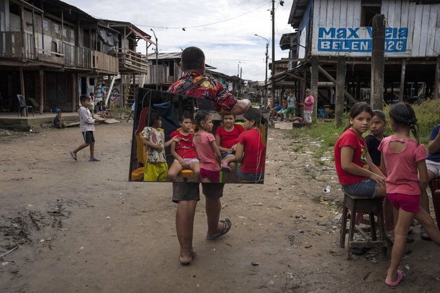 Children are reflected in vendor Manolo Apagueno's mirror as he walks by in the Belen neighborhood of Iquitos, Peru, May 25, 2024. The Indigenous community in the heart of Peru's Amazon known as the "Venice of the Jungle" is hosting the Muyuna Floating Film Festival, celebrating tropical forests. (Photo by Rodrigo Abd/AP Photo)