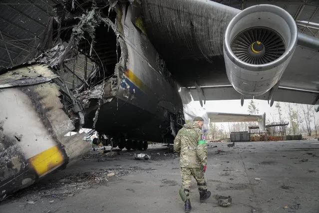 A Ukrainian sapper searches for unexploded explosives as he passes by an Antonov An-225, world's biggest cargo aircraft destroyed during recent fighting between Russian and Ukrainian forces, at the Antonov airport in Hostomel, on the outskirts of Kyiv, Ukraine, Monday, April 18, 2022. (Photo by Efrem Lukatsky/AP Photo)