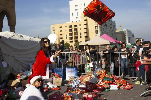 In this Sunday, December 22, 2019, photo, volunteer Ibtisam Nablussi tosses a Christmas present, as anti-government protesters distribute clothing to the needy ahead of Christmas, at Martyrs Square in Beirut, Lebanon. Lebanon is entering its third month of protests, the economic pinch is hurting everyone, and the government is paralyzed. So people are resorting to what they've done in previous crises: They rely on each other, not the state. (Photo by Maya Alleruzzo/AP Photo)