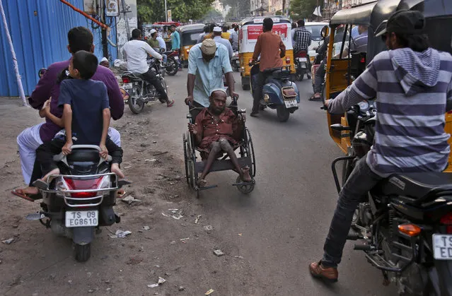 Polio affected Indian man Mastan (60) moves on a wheel chair with the help of another man through a crowded street in Hyderabad, India, Wednesday, June 15, 2016. The city of nearly 7 million people in southern India has declared a “high alert” for polio after an active strain of the virus was found in samples of sewage water, an official said Wednesday. (Photo by Mahesh Kumar A./AP Photo)