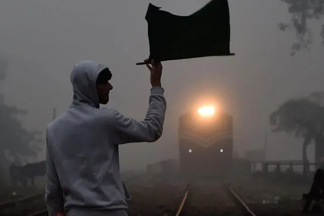 A signalman waves a flag as a train approaches at a station during a cold and foggy morning in Lahore on December 16, 2019. (Photo by Arif Ali/AFP Photo)