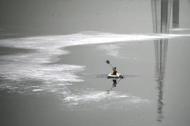A boy rows a boat across the polluted waters of river Yamuna laden with foam, on a hot summer day in New Delhi on June 9, 2022. (Photo by Money Sharma/AFP Photo)