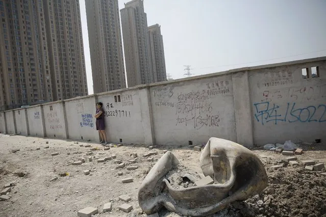A woman evacuated from a residential area looks at a large metal object that landed and damaged the road about two kilometres from the explosion site in Binhai new district in Tianjin, China August 13, 2015. (Photo by Damir Sagolj/Reuters)